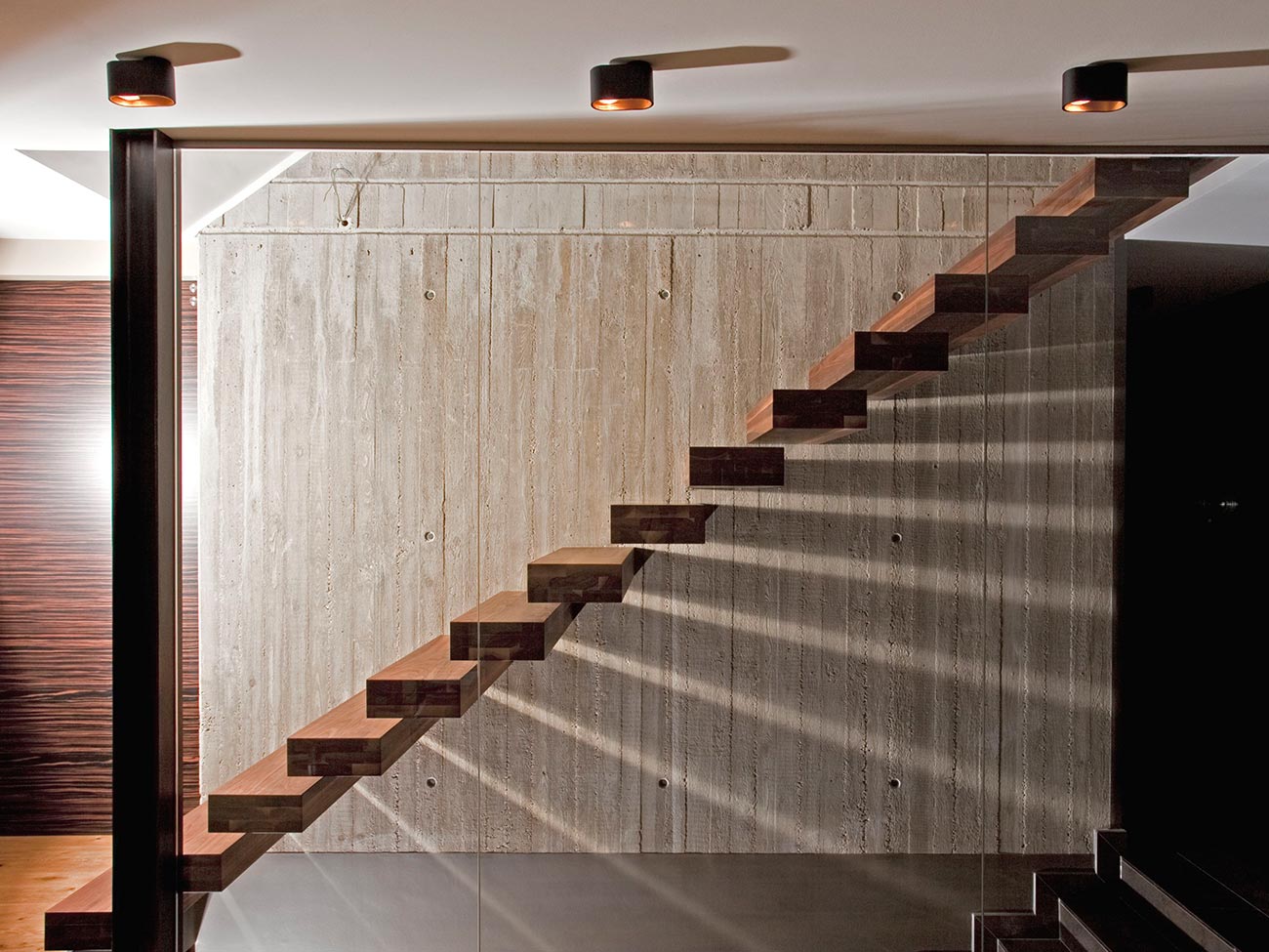 Kragarmtreppe an Betonwand als spannender Designkontrast in hochwertigem Holz