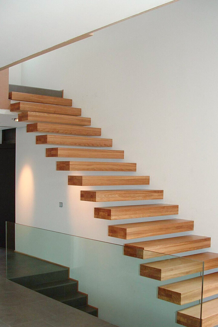 Eine schlichte und elegante Kragramtreppe mit scheinbar freistehenden Stufen aus Holz mit einer Absturzsicherung aus Glas als Glasscheibe