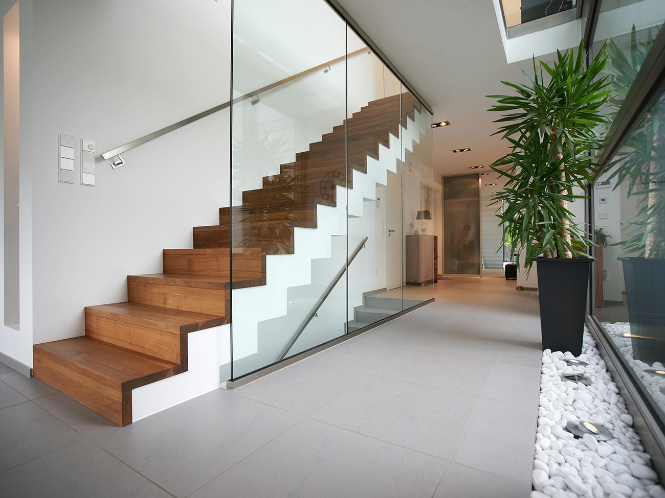 Helle und moderne Betontreppe, in weiß mit eleganten Holzbrettern, Handlauf aus Edelstahl und Glasscheiben vom Boden bis zur Decke