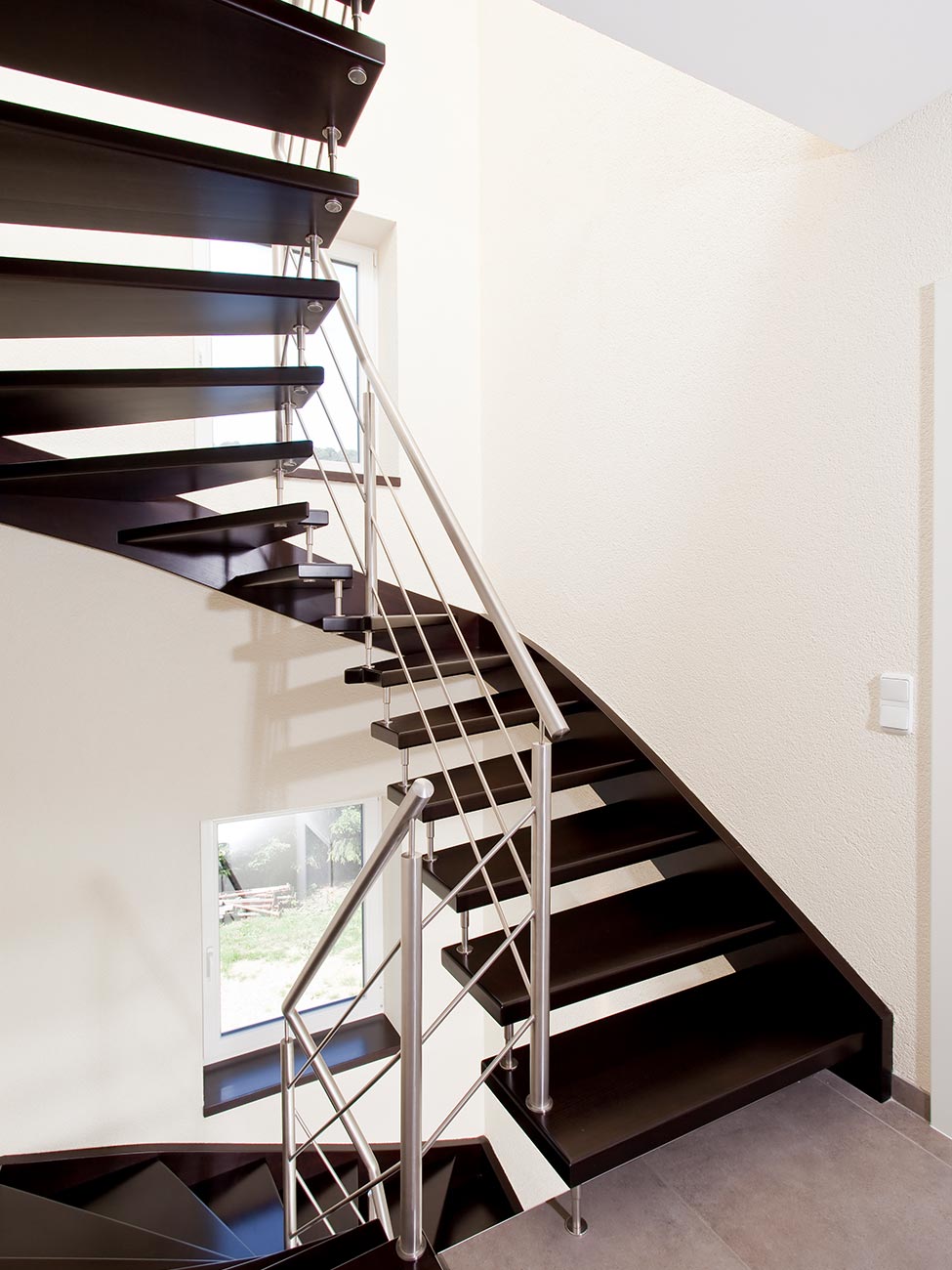Schwarze Thummtreppe mit Metallbolzen und silbernem Geländer, gebogene Treppe