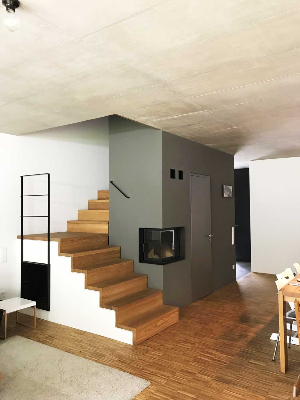 Treppenstufen aus Holz auf Beton die in einem offenen raumkonzept mit einem kleinen Handlauf nach oben führen, perfekt in die Raumfunktion integriert
