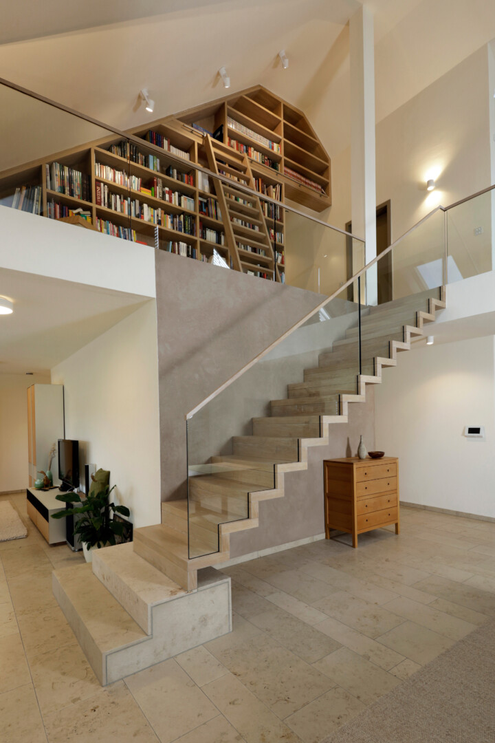 Eine Faltwerktreppe aus Holz mit Geländerscheiben aus Glas, stehend auf einem Sockel